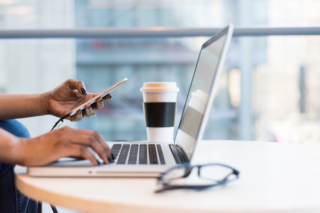 A person is using their phone while sitting at his laptop.