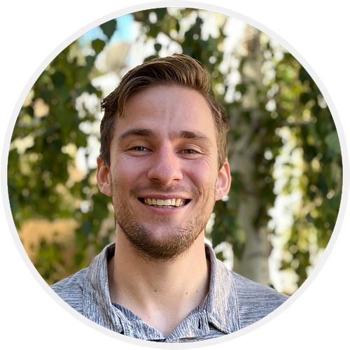 A man smiling for the camera in front of trees.