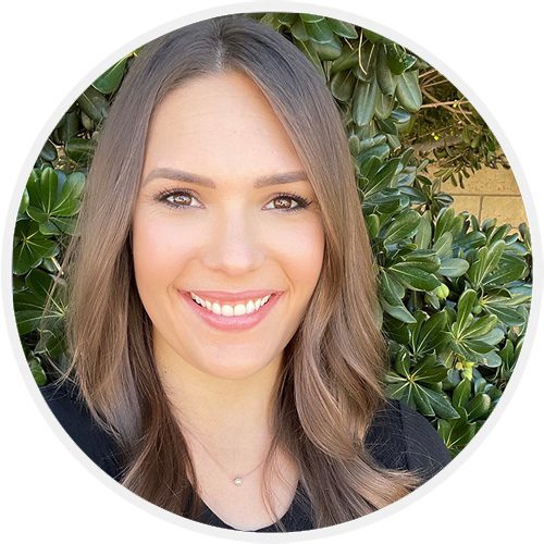 A woman smiling for the camera in front of bushes.