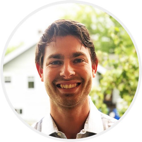 A man smiling for the camera in front of trees.